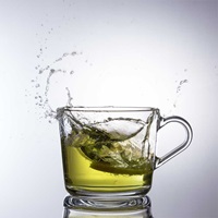 Objektfoto von einer Glastasse mit Grünen Tee in die eine Zitrone fällt